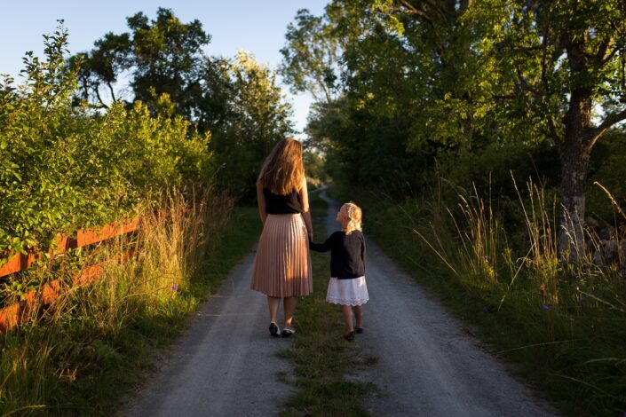 Beautiful green fields and country road. Assumed mother and daughter look at each other and hold hands, walking down the road. The article is about parenting orders and living one parent and spending time with the second.