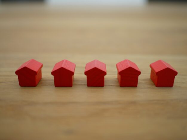 A row of wooden, red houses (six) on a wooden (brown) table. The article discusses property settlement orders for cash payment, refinance and superannuation splits.