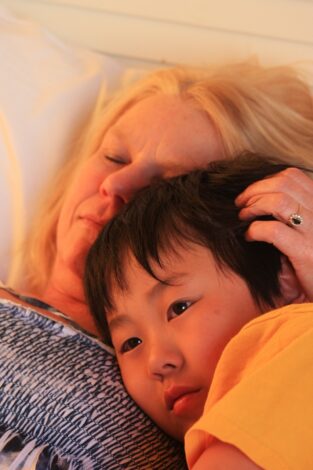 Caucasian Mother lays on the bed with her adopted Asian son. Adoption legal advice helped the process. They look content and relaxed.